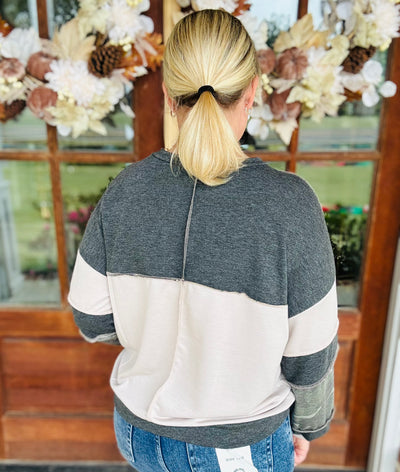 Person wearing a gray and beige color-blocked sweater with a decorative background.